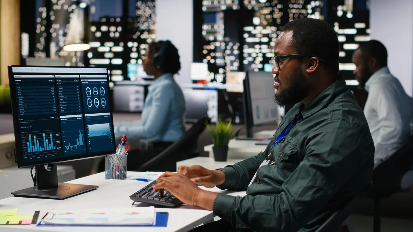 Офисный сотрудник изучает метрики KPI на мониторе и аналитику на рабочем столе, формируя видение и